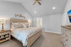 Carpeted bedroom featuring ensuite bathroom, ceiling fan, and lofted ceiling