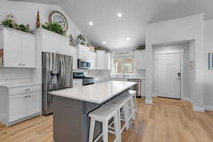 Kitchen with stainless steel appliances, light hardwood / wood-style floors, lofted ceiling, and a center island