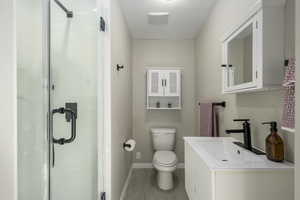 Bathroom featuring toilet, vanity, and a shower with shower door