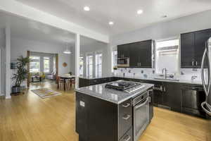 Kitchen with tasteful backsplash, a kitchen island, appliances with stainless steel finishes, pendant lighting, and light hardwood / wood-style floors