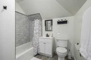 Full bathroom featuring shower / bath combo with shower curtain, wood-type flooring, vanity, lofted ceiling, and toilet