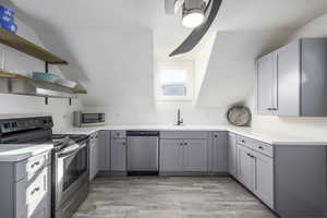 Kitchen with light wood-type flooring, stainless steel appliances, exhaust hood, and gray cabinetry