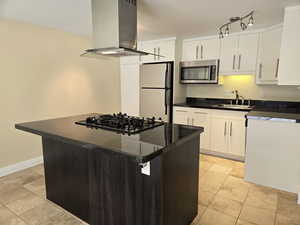 Kitchen with island exhaust hood, white fridge, white cabinetry, gas stovetop, and sink