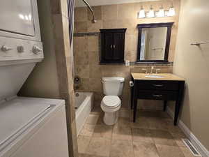 Full bathroom with stacked washing maching and dryer, shower / tub combo with curtain, vanity, and toilet