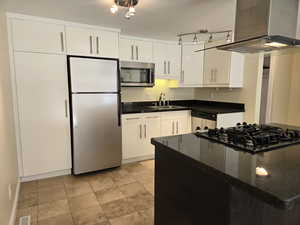 Kitchen with sink, appliances with stainless steel finishes, dark stone countertops, white cabinets, and island exhaust hood