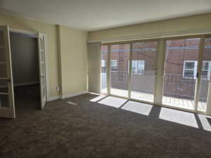 Unfurnished room featuring plenty of natural light and dark carpet