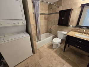 Full bathroom featuring stacked washer and clothes dryer, tile walls, vanity, toilet, and shower / tub combo with curtain