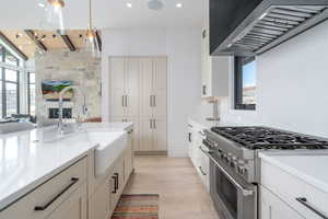 Kitchen featuring a stone fireplace, decorative light fixtures, custom range hood, stainless steel range, and light hardwood / wood-style flooring