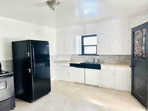 Kitchen featuring decorative backsplash, black fridge, sink, white cabinets, and range