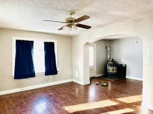 Empty room with hardwood / wood-style floors, ceiling fan, a wood stove, and a textured ceiling