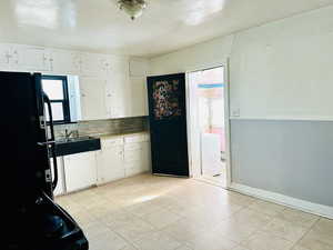 Kitchen featuring tasteful backsplash, black fridge, sink, and white cabinets