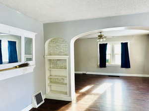 Empty room with built in shelves, ceiling fan, dark hardwood / wood-style floors, and a textured ceiling