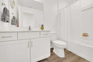 Full bathroom with vanity, hardwood / wood-style floors, shower / bath combo with shower curtain, and toilet