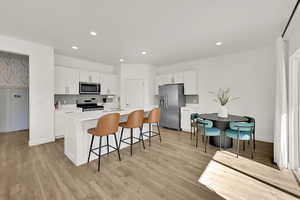 Kitchen with a center island with sink, white cabinets, stainless steel appliances, and light hardwood / wood-style floors