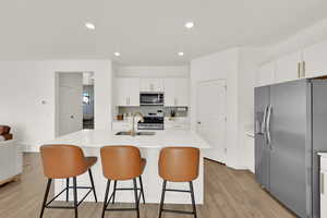 Kitchen featuring a center island with sink, appliances with stainless steel finishes, light wood-type flooring, and white cabinets