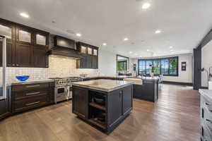 Kitchen with light stone counters, a center island, wood-type flooring, range with two ovens, and wall chimney exhaust hood