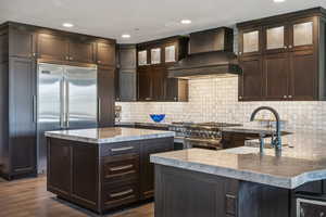 Kitchen with dark hardwood / wood-style flooring, high quality appliances, decorative backsplash, a kitchen island, and wall chimney exhaust hood