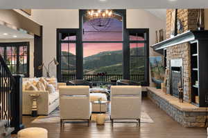 Living room featuring a stone fireplace, an inviting chandelier, a mountain view, wood-type flooring, and vaulted ceiling