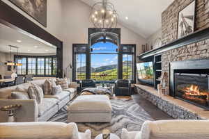 Living room featuring high vaulted ceiling, dark hardwood / wood-style flooring, a stone fireplace, and an inviting chandelier