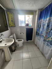 Bathroom with shower / bath combo with shower curtain, tile patterned floors, a textured ceiling, and tile walls