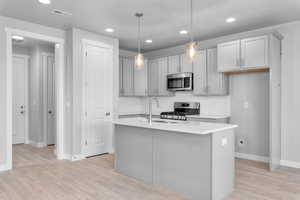 Kitchen featuring decorative light fixtures, an island with sink, light hardwood / wood-style floors, and stainless steel appliances