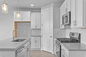 Kitchen featuring stainless steel appliances, hanging light fixtures, and white cabinets