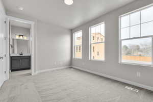 Unfurnished bedroom featuring ensuite bathroom, light colored carpet, and multiple windows