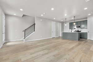 Kitchen featuring hanging light fixtures, a kitchen island with sink, appliances with stainless steel finishes, and light hardwood / wood-style flooring