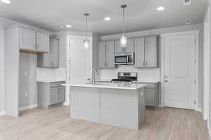 Kitchen featuring stainless steel appliances, sink, decorative light fixtures, a kitchen island with sink, and light wood-type flooring