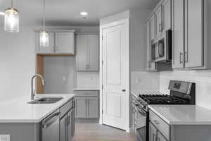 Kitchen with hanging light fixtures, gray cabinets, light hardwood / wood-style floors, and appliances with stainless steel finishes