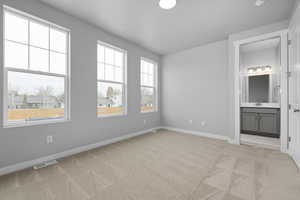 Unfurnished bedroom with ensuite bathroom, light colored carpet, and sink