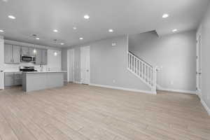 Kitchen with stainless steel appliances, hanging light fixtures, a kitchen island with sink, light hardwood / wood-style flooring, and gray cabinets