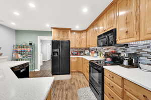 Kitchen with light wood-type flooring, black appliances, and tasteful backsplash