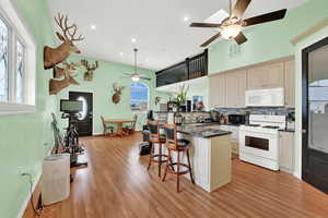 ADU Kitchen featuring light hardwood / wood-style floors, tasteful backsplash, a kitchen breakfast bar, white appliances, and cream cabinetry