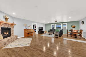 Living room featuring ceiling fan, hardwood / wood-style flooring, and a stone fireplace