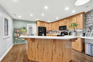 Kitchen with wood-type flooring, decorative backsplash, black appliances, a kitchen island, and light brown cabinets