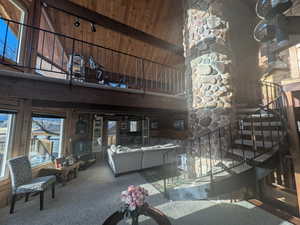 Living room with carpet flooring, high vaulted ceiling, wooden walls, and beamed ceiling