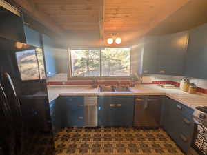 Kitchen with stainless steel appliances, tile countertops, sink, wooden ceiling, and backsplash