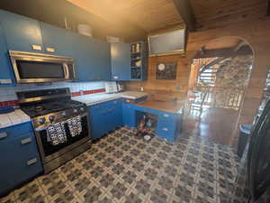 Kitchen featuring beamed ceiling, appliances with stainless steel finishes, decorative backsplash, dark wood-type flooring, and blue cabinets