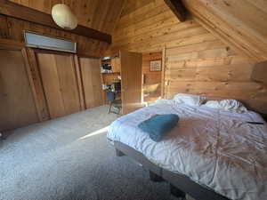 Carpeted bedroom featuring wooden walls and vaulted ceiling with beams