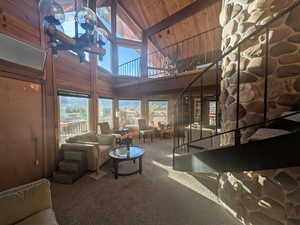 Living room with beam ceiling, high vaulted ceiling, wood ceiling, wooden walls, and carpet floors