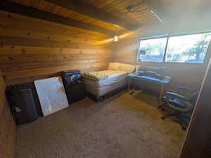 Carpeted bedroom featuring wood walls, beamed ceiling, and wood ceiling