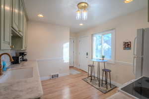 Kitchen featuring sink, white appliances, green cabinets, and light wood-type flooring