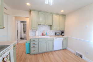 Kitchen with tasteful backsplash, white dishwasher, light hardwood / wood-style floors, and sink