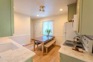 Kitchen with light wood-type flooring, green cabinets, a notable chandelier, and white appliances