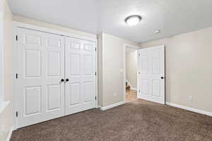 Unfurnished bedroom featuring carpet flooring, a textured ceiling, and a closet