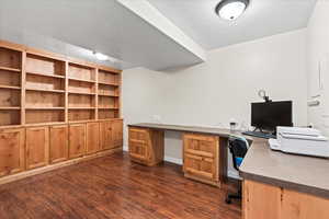 Basement office featuring dark wood-type flooring and built in desk