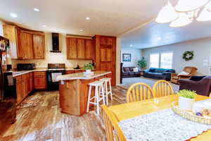 Kitchen featuring a center island, wall chimney exhaust hood, black appliances, light hardwood / wood-style flooring, and decorative light fixtures