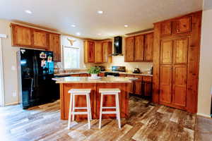 Kitchen with hardwood / wood-style floors, wall chimney exhaust hood, black appliances, and a kitchen island