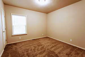 Empty room with a textured ceiling and carpet flooring